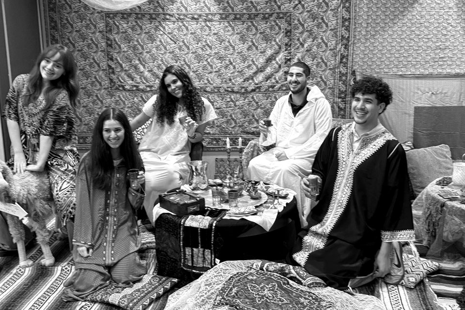 Students in traditional Moroccan dress gather on cushions around a tea table.