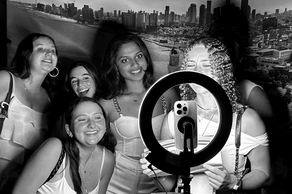 Students pose at a photo booth in front of a backdrop of the Tel Aviv skyline.