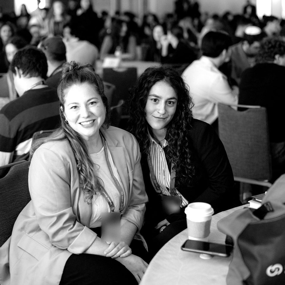 Two students at a front table at the Summit, the full ballroom behind them.